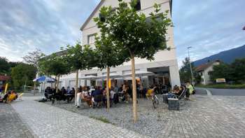 Lively terrace of the St. Martins Pub am Platz with shady trees and guests at tables
