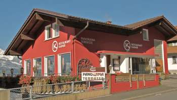 Red building of the Kainer restaurant with wooden balcony and inviting outdoor area