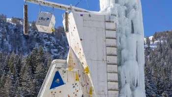 Frozen ice tower in Malbun with visible climbing routes and belay points, against a blue sky
