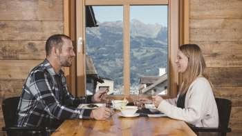 A couple enjoys a cozy meal with a mountain view in a rustic wooden setting