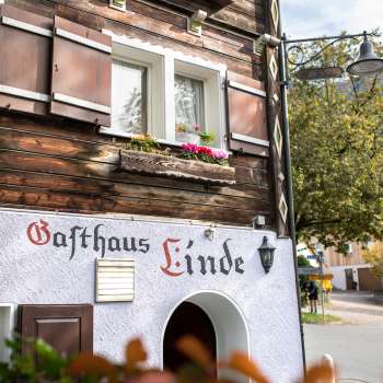 Façade of the Gasthaus Linde with rustic timber construction and shutters, decorated with flowers.