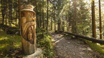 Wooden figure with lantern on the Walser Saga Trail in the mystical forest light