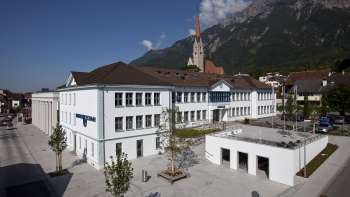 The Domus building in Schaan with its white façade and view of the parish church - a cultural center and meeting place in the heart of Liechtenstein