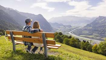 Two hikers sit on a bench and enjoy the view of the Rhine Valley