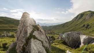 Sunrise behind rock formations in the green Naaftal valley in Liechtenstein, surrounded by rolling hills and mountain scenery