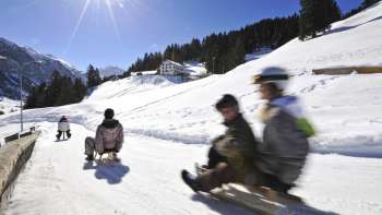 Teachers tobogganing the toboggan run on a beautiful sunny day in the winter landscape