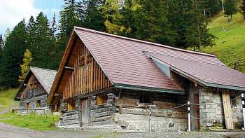 Historic wooden building of the old youth hostel in Malbun in front of a wooded mountainside.