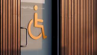 Orange wheelchair symbol on a glass door indicating an accessible toilet, with wood paneling in the background.