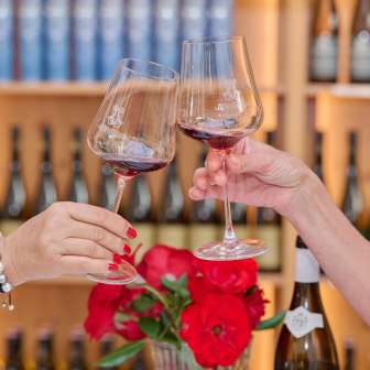 Two women toast with red wine in the Court Winery of the Prince of Liechtenstein, wine racks with fine wines in the background