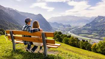 Couple on a wooden bench with a view of the Rhine Valley and the mountains.