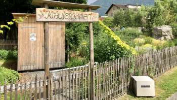 Wooden sign with the inscription "Kräutergarten" (herb garden) at the entrance to the lovingly landscaped garden in Mauren, surrounded by nature and mountains.