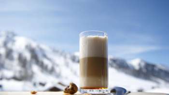 Glass of latte macchiato on a wooden platter against the backdrop of snow-covered mountains