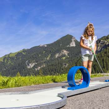 Girl concentrates on a blue looping course in an alpine setting while playing mini golf