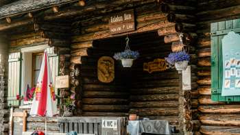 Entrance area of the hut: Rustic entrance area of the Gafadura hut with wooden facade, colorful flowers and information board