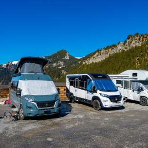 Several campers and motorhomes on a pitch in the mountains of Liechtenstein under a bright blue sky
