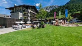 Family-friendly Hotel Gorfion in Malbun with a large play area and mountain backdrop in summer