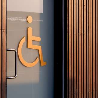 Orange wheelchair symbol on a glass door indicating an accessible toilet, with wood paneling in the background.