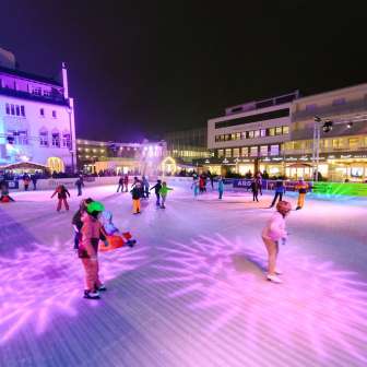 People ice skating on the illuminated ice rink of Vaduz on Ice in the city center of Vaduz in the evening