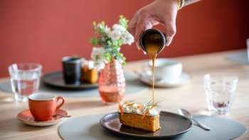 Dessert is topped with caramel sauce, coffee cups and stylish table decorations in the background