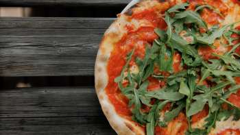 Fresh pizza with tomato sauce and rocket, served on a rustic wooden table