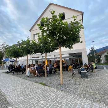 Lively terrace of the St. Martins Pub am Platz with shady trees and guests at tables.