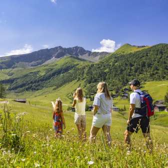 A family walks through a blooming summer meadow in Malbun, Liechtenstein, and enjoys the view of the surrounding Alps.
