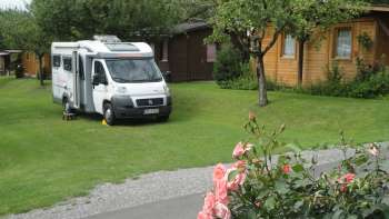Motorhome pitch at the Mittagsspitze campsite with green meadow and surrounding wooden huts.
