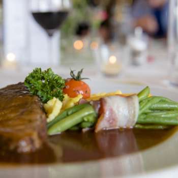 Close-up of a main course with green vegetables, bacon and creamy sauce on the plate