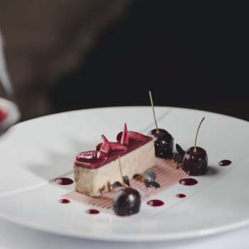 Elegant dessert on a white plate, decorated with cherries and chocolate