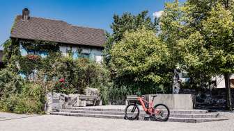 Red e-bike in front of a historic building in Liechtenstein, surrounded by trees and fountains, ideal starting point for a bike tour through the country