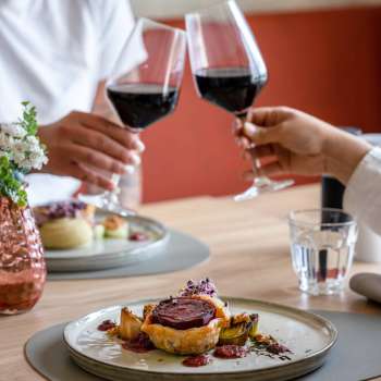 Two people toast with red wine, in the foreground a lovingly prepared main course