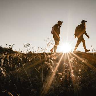 Two hikers in Liechtenstein at sunset, silhouette on a mountain path with a natural meadow in the foreground