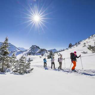Group snowshoe hiking through the snow-covered landscape on Schönberg mountain near Malbun under the bright winter sun.