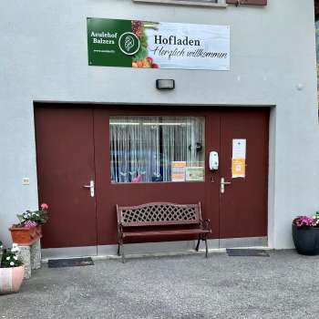 Entrance to the Aeulehof farm store with red gate, bench and floral decorations in Triesen, Liechtenstein.