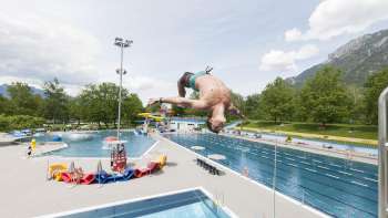 A boy does a somersault from the diving platform into the pool