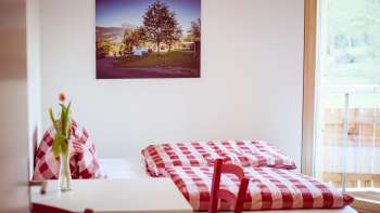 Cozy double room in the guest house at Camping Mittagsspitze with red and white checkered bed linen and decoration.