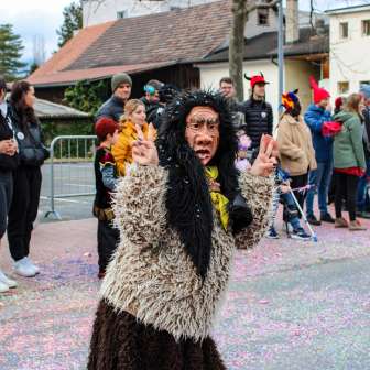 Disguised Schaan witch at the carnival parade in Schaan, Liechtenstein, in front of an audience and colorful confetti on the street