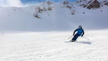 Skiers on a wide ski slope in Malbun, Liechtenstein, surrounded by snow-covered Alpine slopes and a bright blue sky