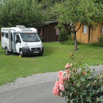 Motorhome pitch at the Mittagsspitze campsite with green meadow and surrounding wooden huts.