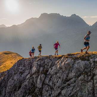 Group of trail runners on a rocky ridge in the mountains of Liechtenstein in the morning sun and impressive alpine scenery