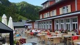 Sunny terrace of the restaurant with covered tables, parasols and views of the Alps.