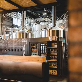 Interior view of a brewery with stainless steel brewing system and inviting bar in the foreground.