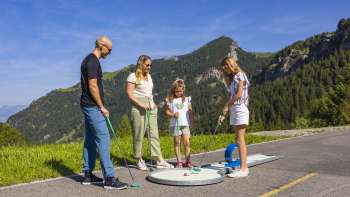  Family playing minigolf together in the mountains of Malbun in bright sunshine