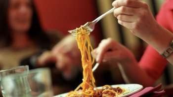 A person lifts spaghetti with a fork from a plate in the Brasserie Burg - Italian enjoyment in a convivial atmosphere.