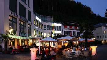 Evening atmosphere in front of the Brasserie Burg in Vaduz with illuminated terrace and guests under parasols.