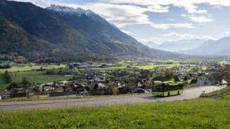 Green LIEmobil bus drives along a winding road above Liechtenstein with a view of the Rhine Valley and the surrounding Alps