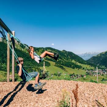 Two children swinging with a view of Malbun