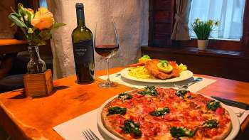 Close-up of a pizza with tomatoes, cheese and basil on a wooden table, with a glass of red wine in the background.
