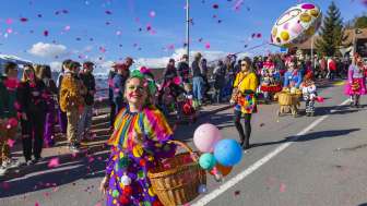 Clown dressed up with confetti and balloons at the carnival parade, spectators on the roadside.