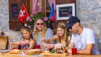 Family sitting on a sunny alpine pasture in Liechtenstein and enjoying a traditional snack with regional specialties and a mountain panorama